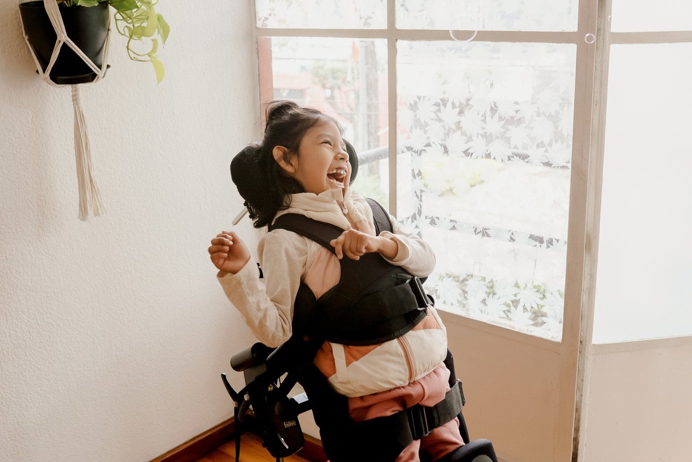 Young girl in wheelchair laughing joyfully by a window at home